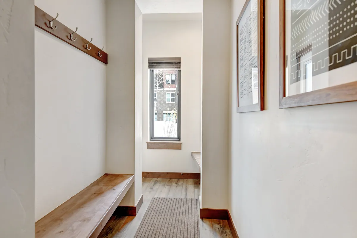 A welcoming entry area with coat hooks, a bench for putting on or taking off shoes, a window letting in natural light, and framed artwork adorning the walls. The space feels inviting and practical, perfect for transitioning between outdoor and indoor activities.