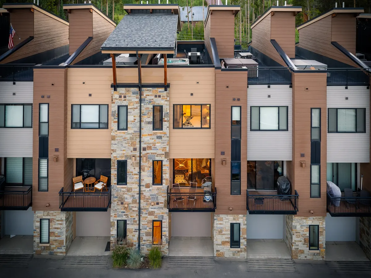 A welcoming exterior view of the townhome's stone facade, large windows, and inviting balconies furnished for outdoor lounging. The image hints at the home’s modern style and its integration with the lively downtown environment.