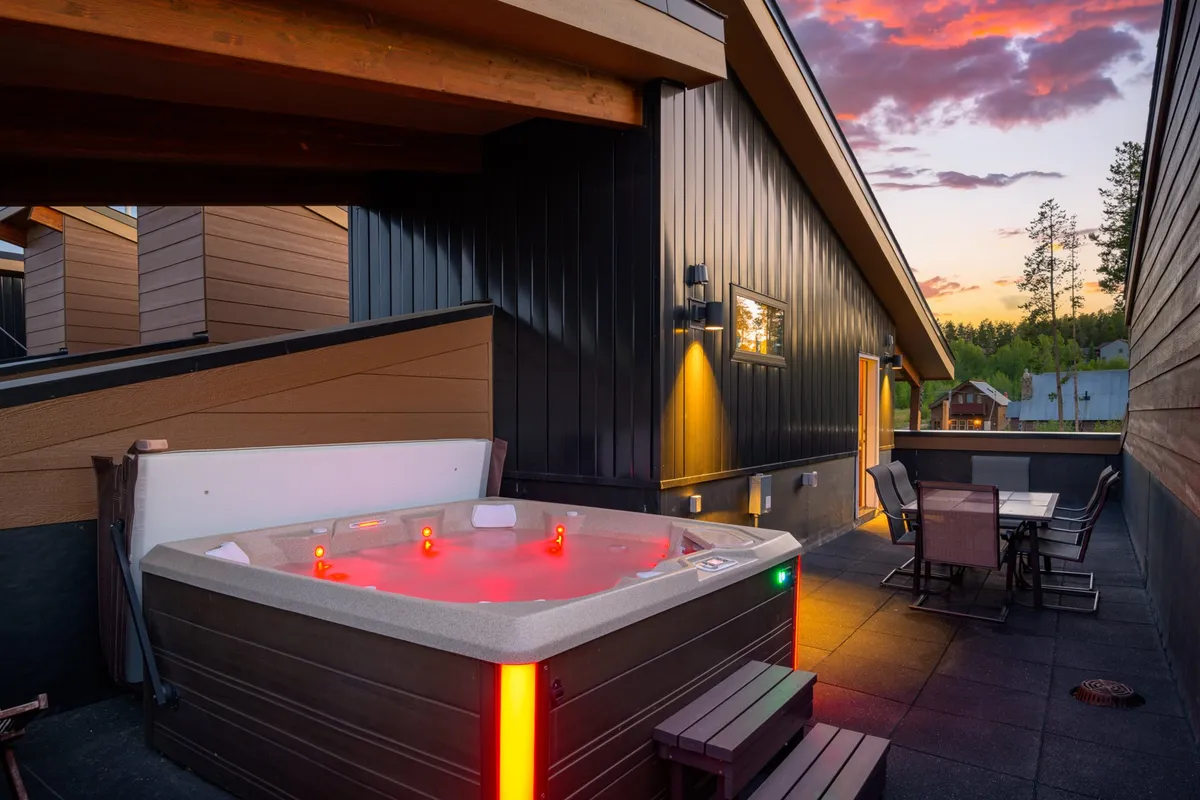An exterior shot featuring the rooftop hot tub, an outdoor dining set, and soft lighting fixtures. The setting is ideal for both relaxation and social gatherings, highlighting the multi-use aspect of the patio—perfect for dining, unwinding under the stars, or sharing stories with friends.
