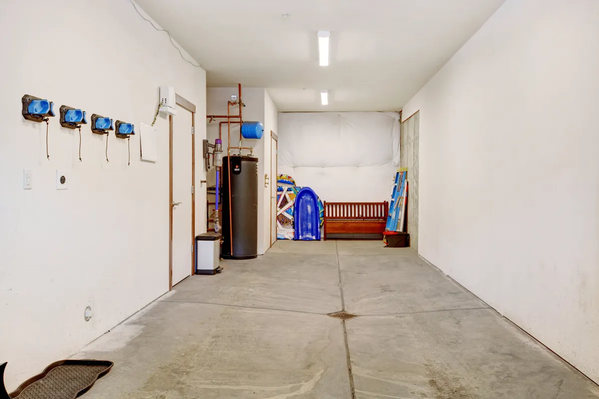 This image features a well-organized utility space with blue wall-mounted electrical outlets, a water heater, wooden bench, blue sled, and a ladder. The scene is functional, highlighting gear storage and seasonal equipment organization.