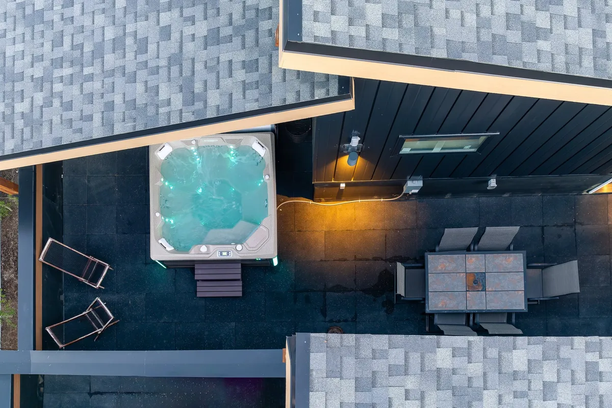 An inviting exterior shot featuring a hot tub on the rooftop patio, surrounded by an outdoor dining table and spacious patio area. The scene conveys relaxation, group gatherings, and the enjoyment of starlit evenings.
