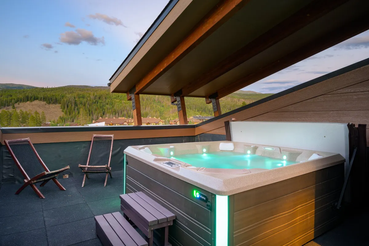 A private deck with a hot tub overlooking stunning mountain views, complemented by deck chairs for relaxation. The tranquil setting suggests opportunities for soaking under the stars, admiring sunsets, and enjoying intimate gatherings.