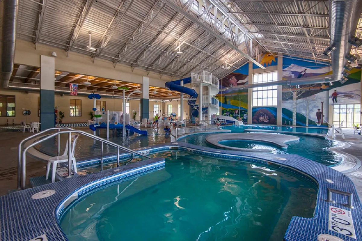 A lively indoor recreation center with water slides, pool areas, bright murals, and children playing. The atmosphere buzzes with activity and fun, showing a vibrant community amenity for families and adventurers alike.
