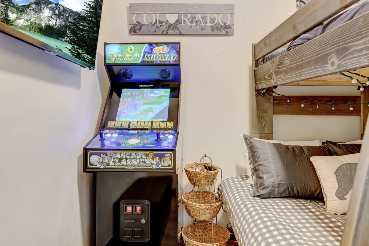 A playful and inviting bunk room with an arcade game machine, bunk bed, and decorative elements. The room is designed for fun and flexibility, ideal for families or groups with children, and supports late-night gaming or cozy movie nights.