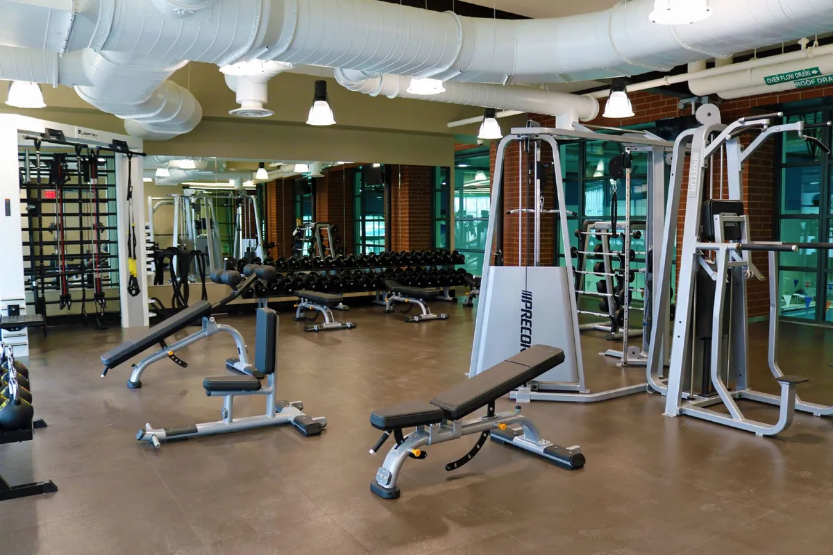A well-equipped fitness area featuring weight lifting equipment, dumbbell racks, and exercise benches, exuding a motivational ambiance for personal training or group workouts. It suggests access to high-quality resort-style amenities and wellness opportunities for guests year-round.