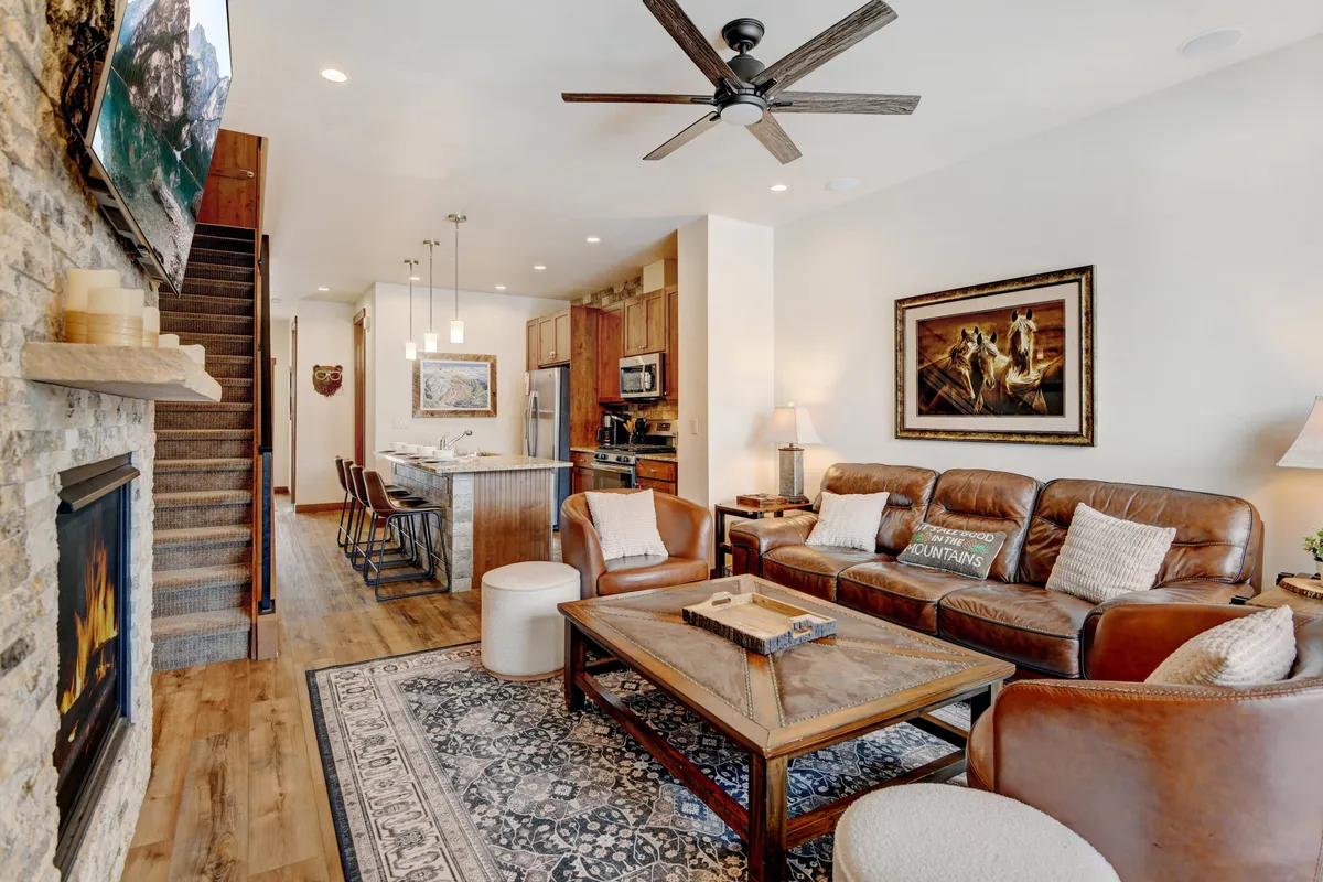A welcoming perspective of the central living and dining space, featuring a plush sofa set, a glowing fireplace, a spacious dining table, and a staircase leading upstairs. The room is designed for relaxation and group activities, with ample space for everyone to unwind or come together after a day’s mountain adventures.