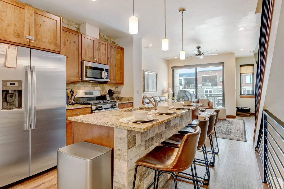 A stylish chef’s kitchen with a large island and seating, stainless steel appliances, artistic touches, and a prominent window pouring natural light into the space. The kitchen is designed for both culinary creativity and group interaction, inviting guests to gather around the island for meals, games, or conversation.