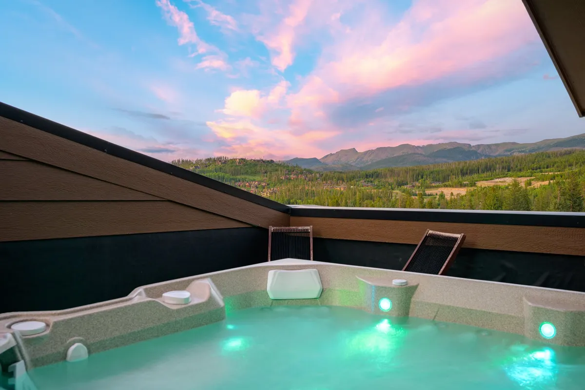 This exterior image showcases a private rooftop hot tub with spectacular mountain views under a sunset sky. The scene emanates tranquility and invites the viewer to imagine relaxing in the warm water, surrounded by natural beauty as day turns to night.