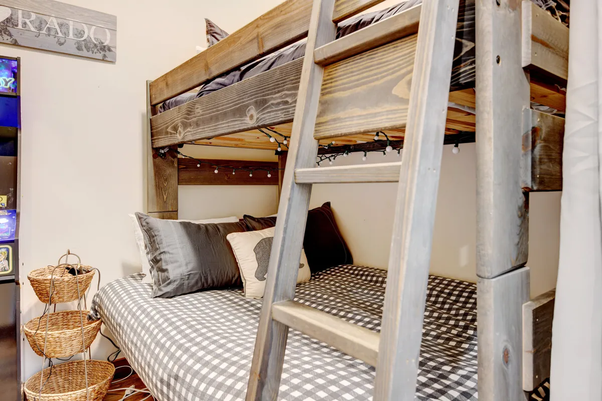 A cheerful, playful bunk bedroom with a ladder, checkered bedding, decorative pillows, and a shelf with baskets, evoking a cozy, inviting space for children to relax, read, and play together.